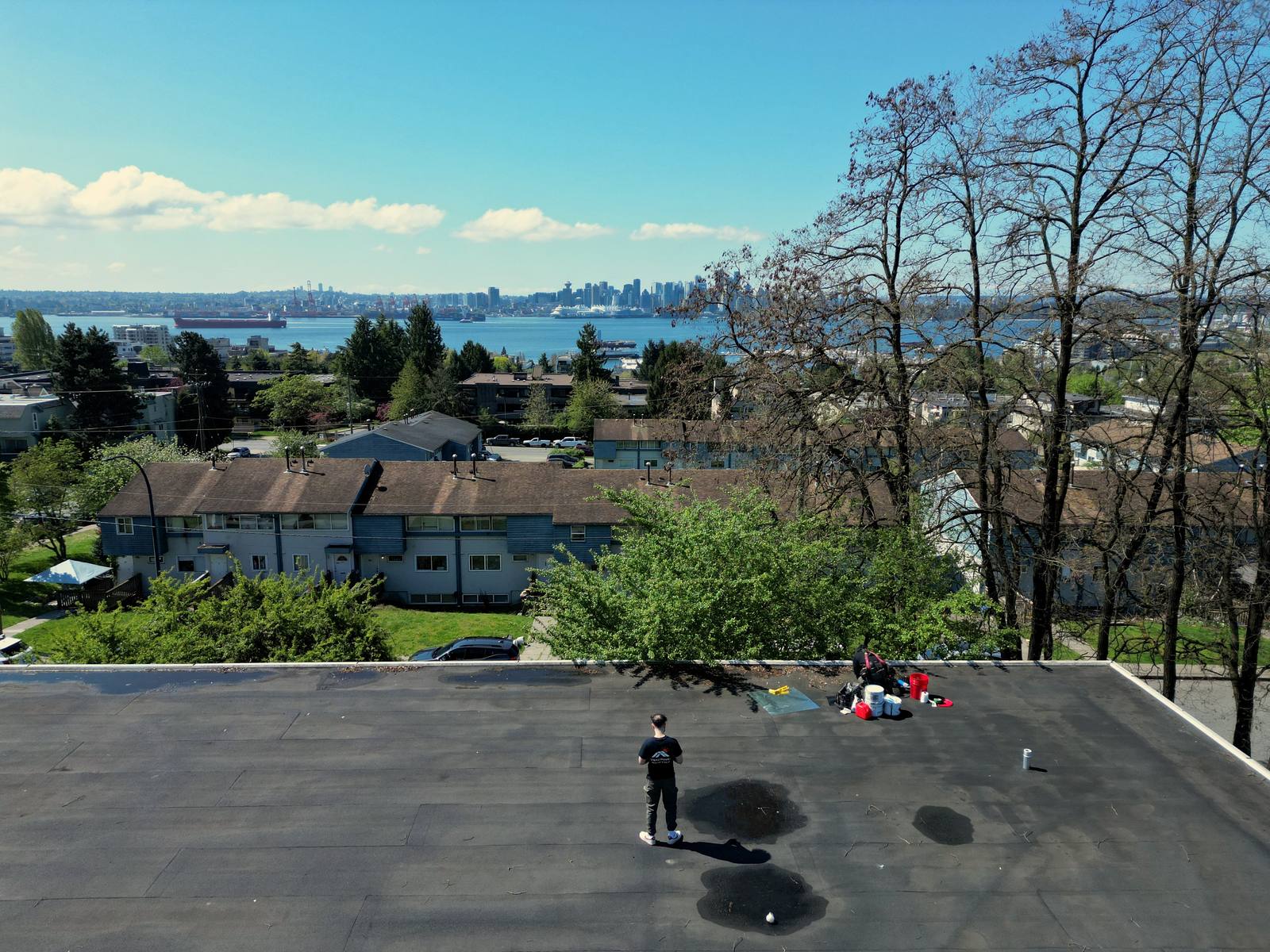 Vancouver Roofing & Solar crew working a flat roof overlooking Burrard Inlet and the downtown Vancouver skyline